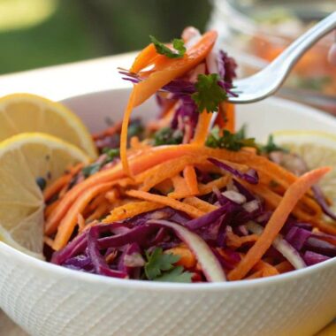 A close-up image of a colorful raw sweet potato salad garnished with lemon wedges.