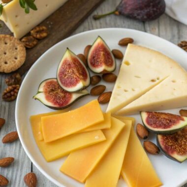 A close-up of Gouda cheese slices on a platter with figs, almonds, and crackers, showcasing its creamy texture and golden color.