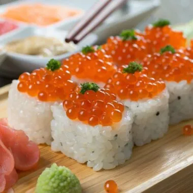 Close up of Ikura sushi with bright orange salmon roe on top, garnished with wasabi and pickled ginger