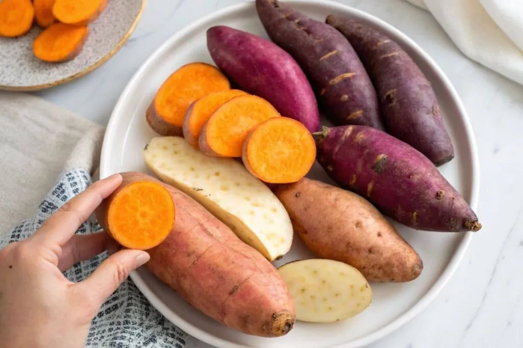 An elegant arrangement of sweet potatoes with orange, white, and purple varieties displayed on a clean white plate.