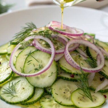 A close-up of fresh Persian cucumbers sliced thin, served in a vibrant salad with dill, red onion, and a drizzle of olive oil on a white plate