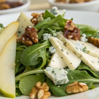 Fresh salad with Roquefort cheese crumbles, mixed greens, pears, and walnuts on a white plate.