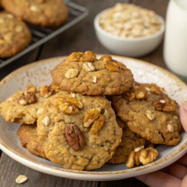 A close-up image of oatmeal cookies with walnuts and sunflower seeds, held in hand