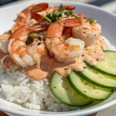 A shrimp poke bowl with cooked shrimp, rice, cucumber, and spicy mayo